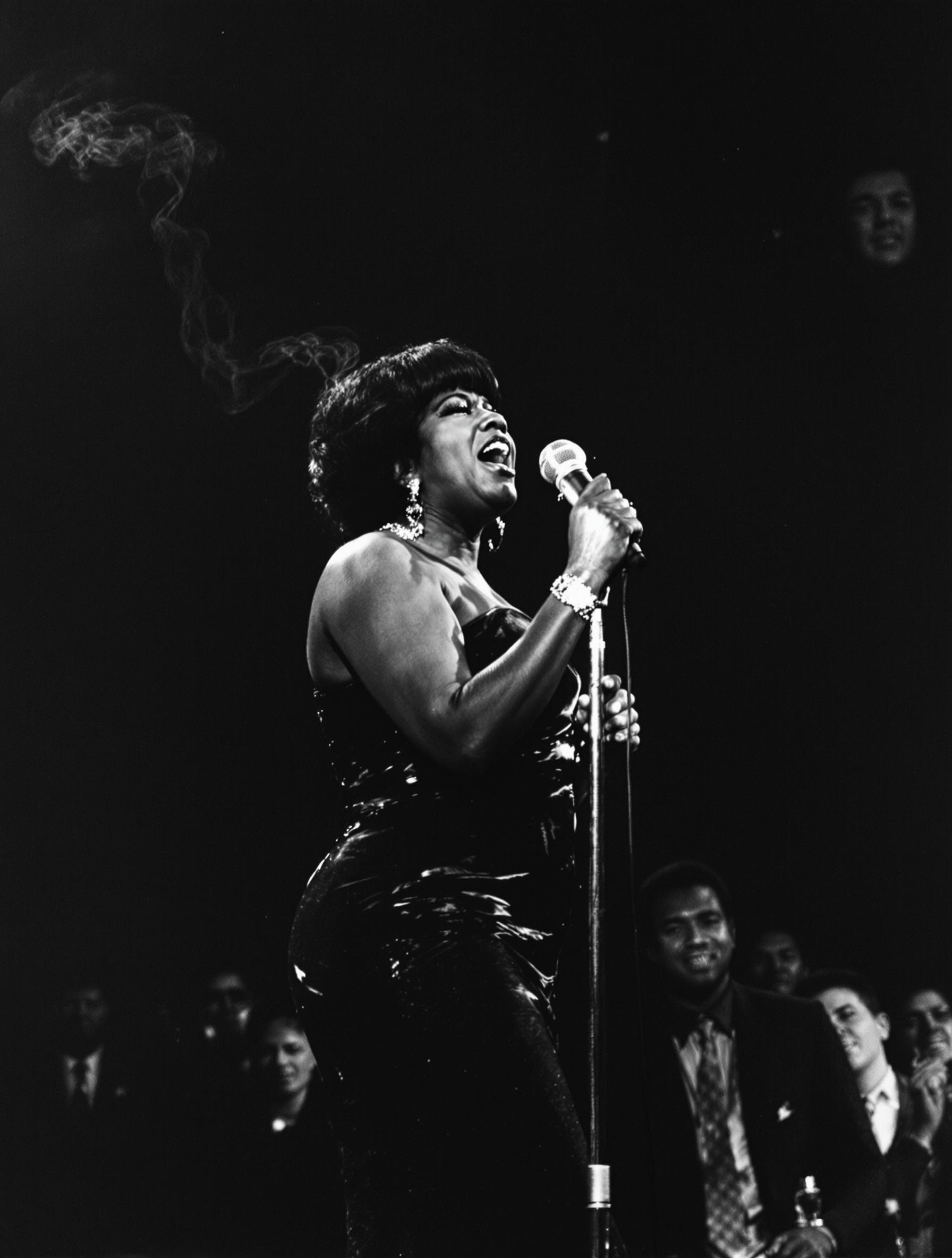 Aretha Franklin sur scène en 1968, robe élégante, micro vintage RCA à la main durant un concert marquant pour la révolution soul et les droits civiques.