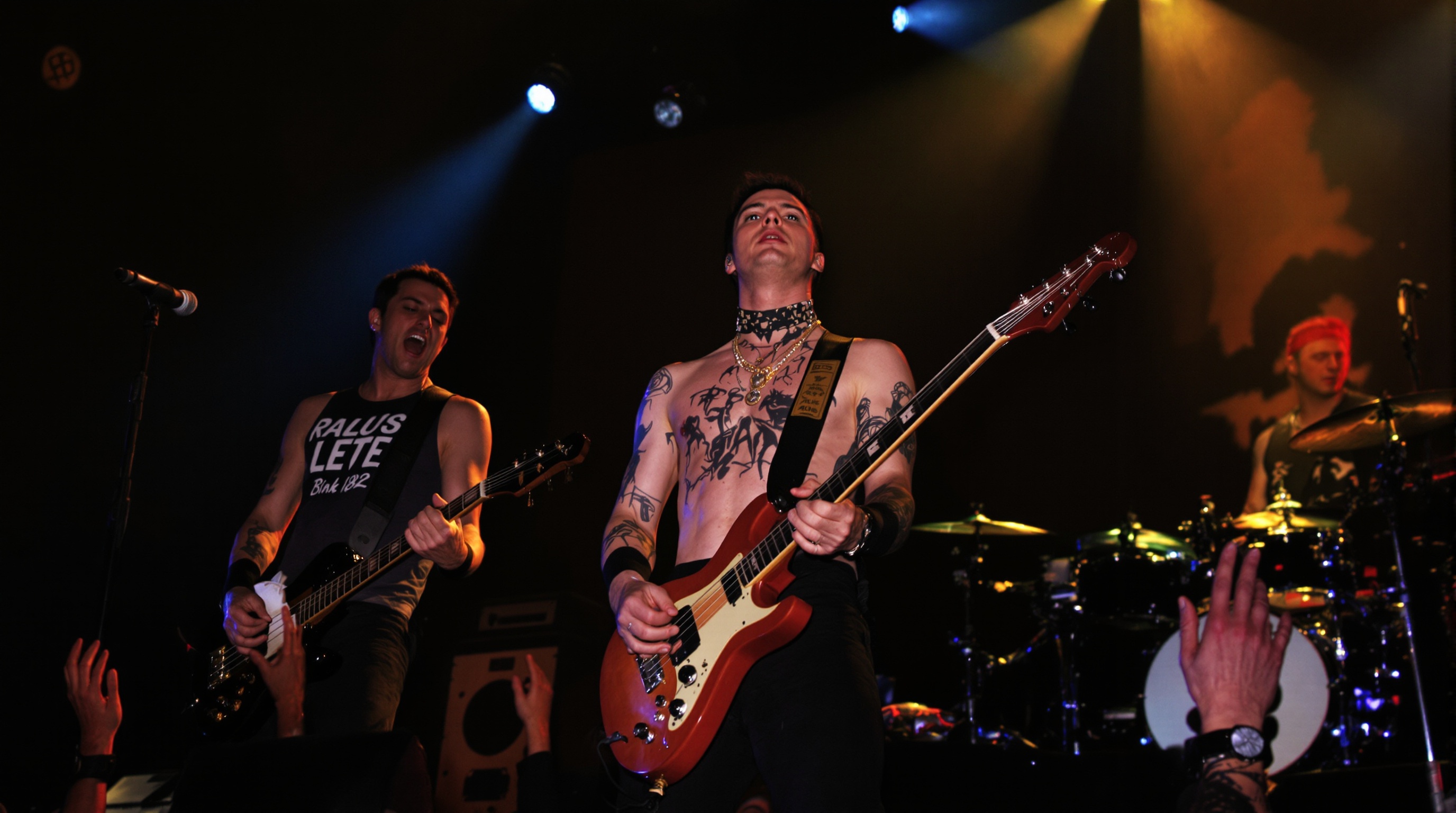 Image iconique du trio original de Blink-182, Tom DeLonge, Mark Hoppus et Travis Barker, capturant leur énergie juvénile et leur complicité sur scène.