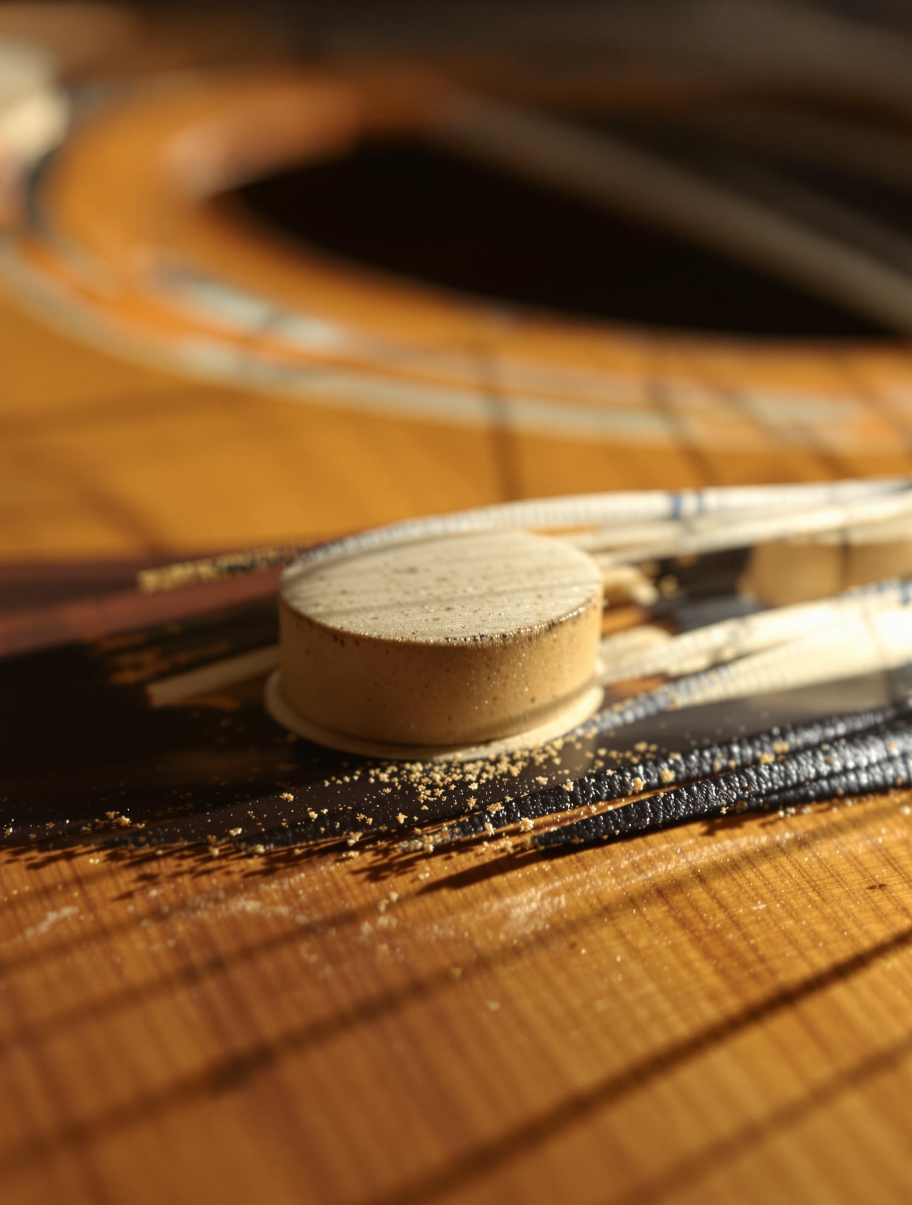 Macro photo poétique du sillet d'une guitare classique sous tension, montrant la différence de courbure des cordes selon trois tensions