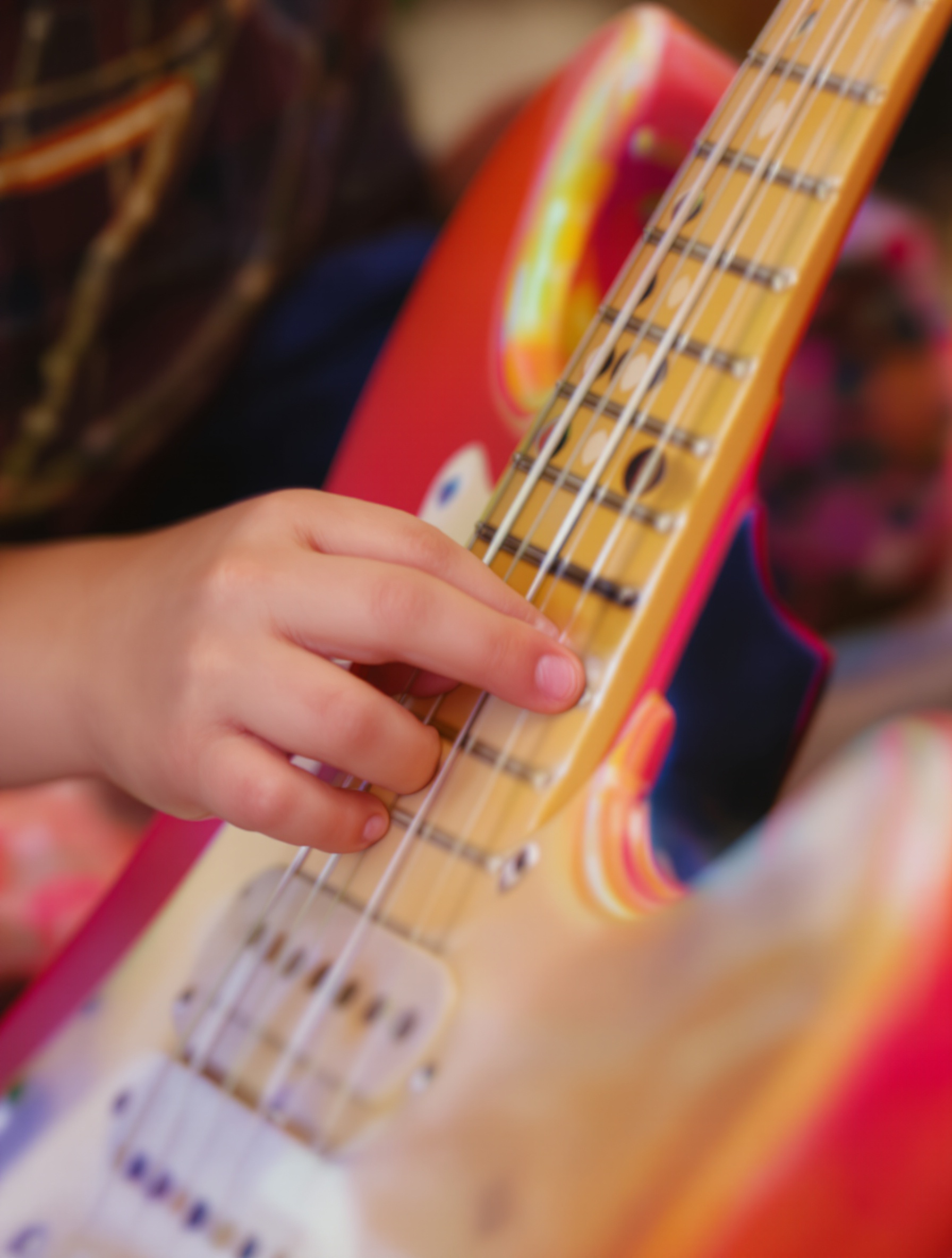 Petites mains d'un enfant explorant les frettes d'une guitare électrique 1/2 colorée