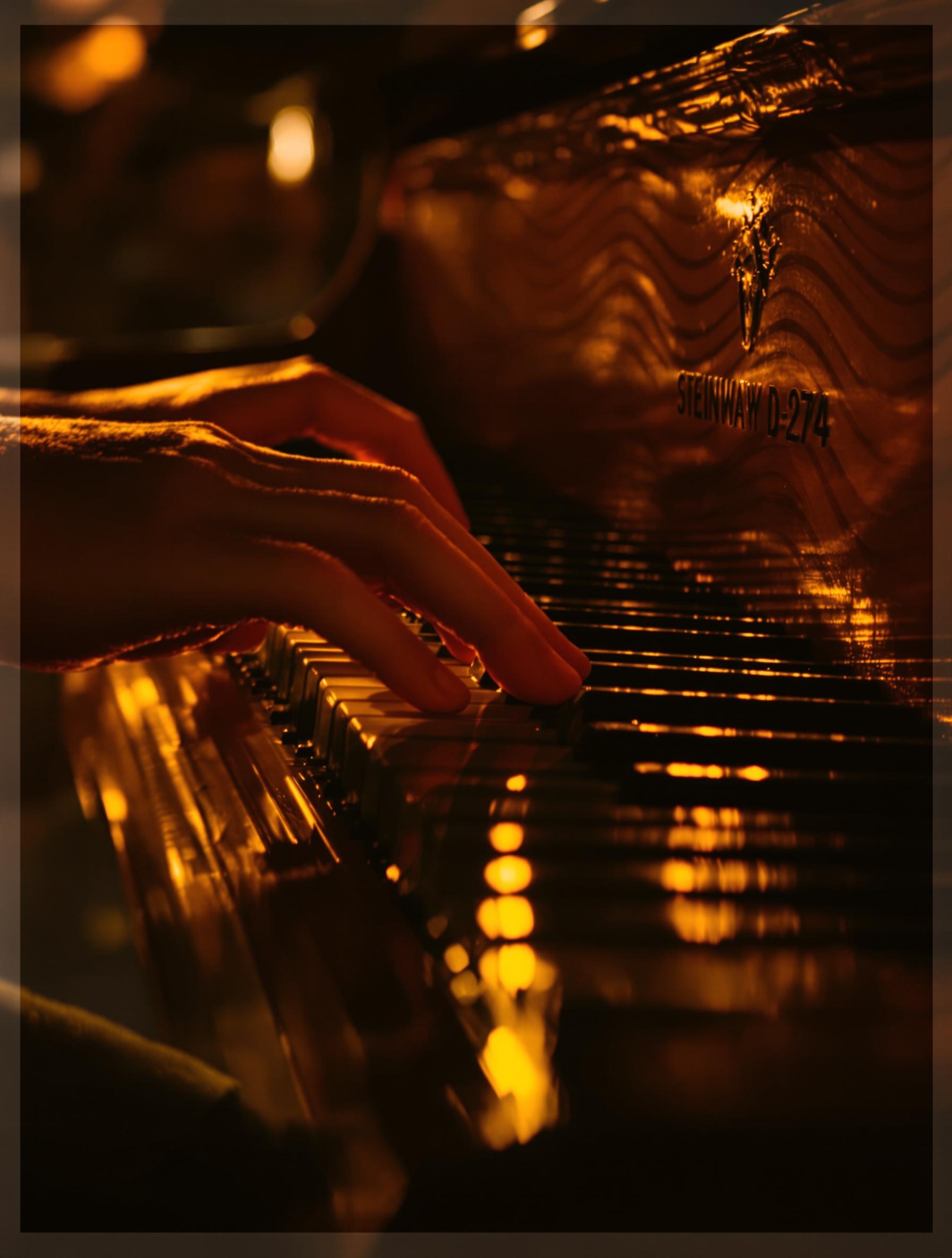 Mains effleurant le clavier d’un Steinway D-274 sous une lumière dorée, ambiance patrimoniale.